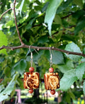 Pair of earrings with brown square beads and red beads hanging on a branch with green leaves.