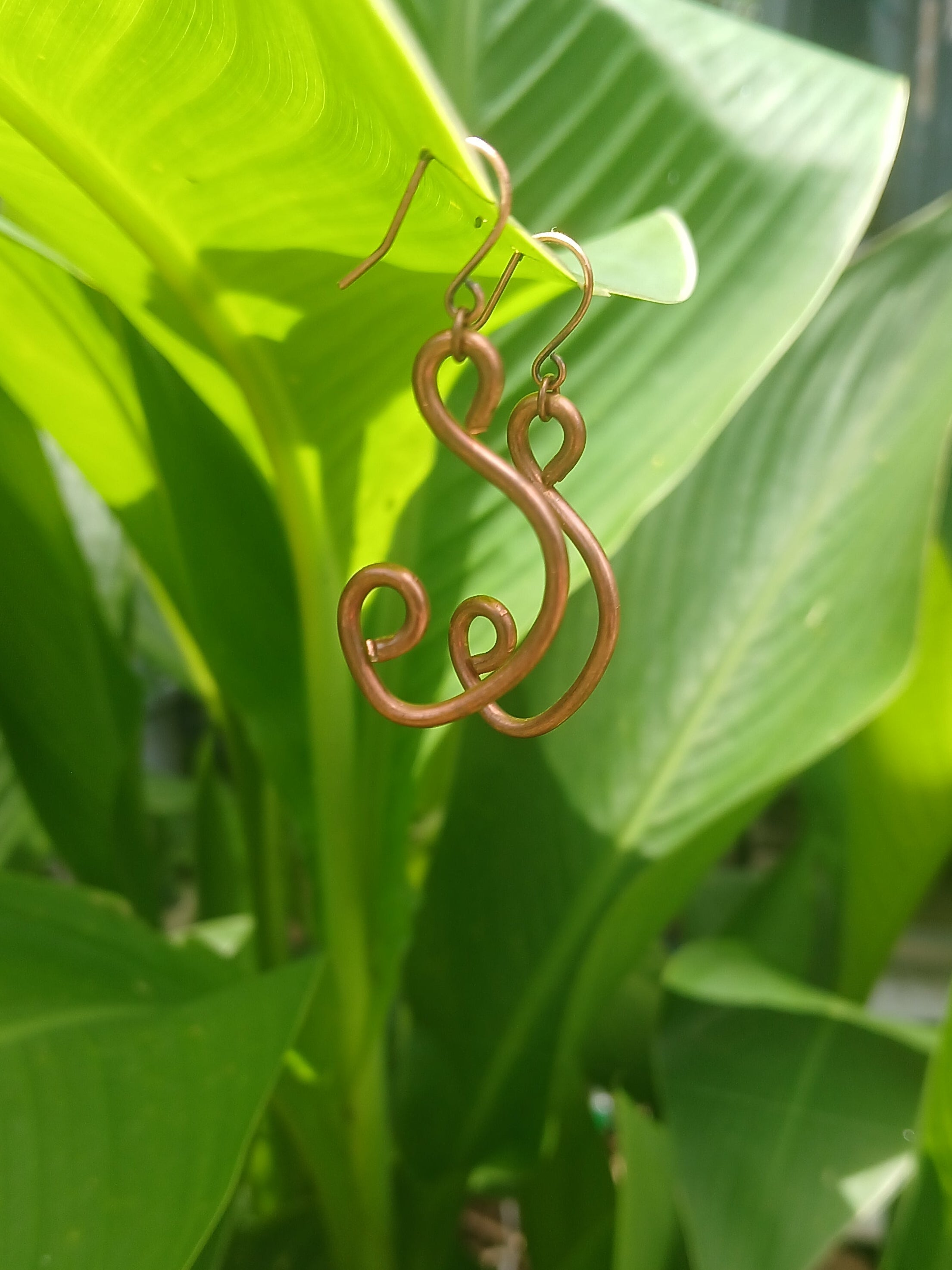 Decorative copper plant hanger on a green leafy background