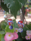 Pair of earrings with colorful beads hanging on a leaf with flowers in the background