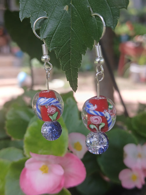 Pair of earrings with colorful beads hanging on a leaf with flowers in the background