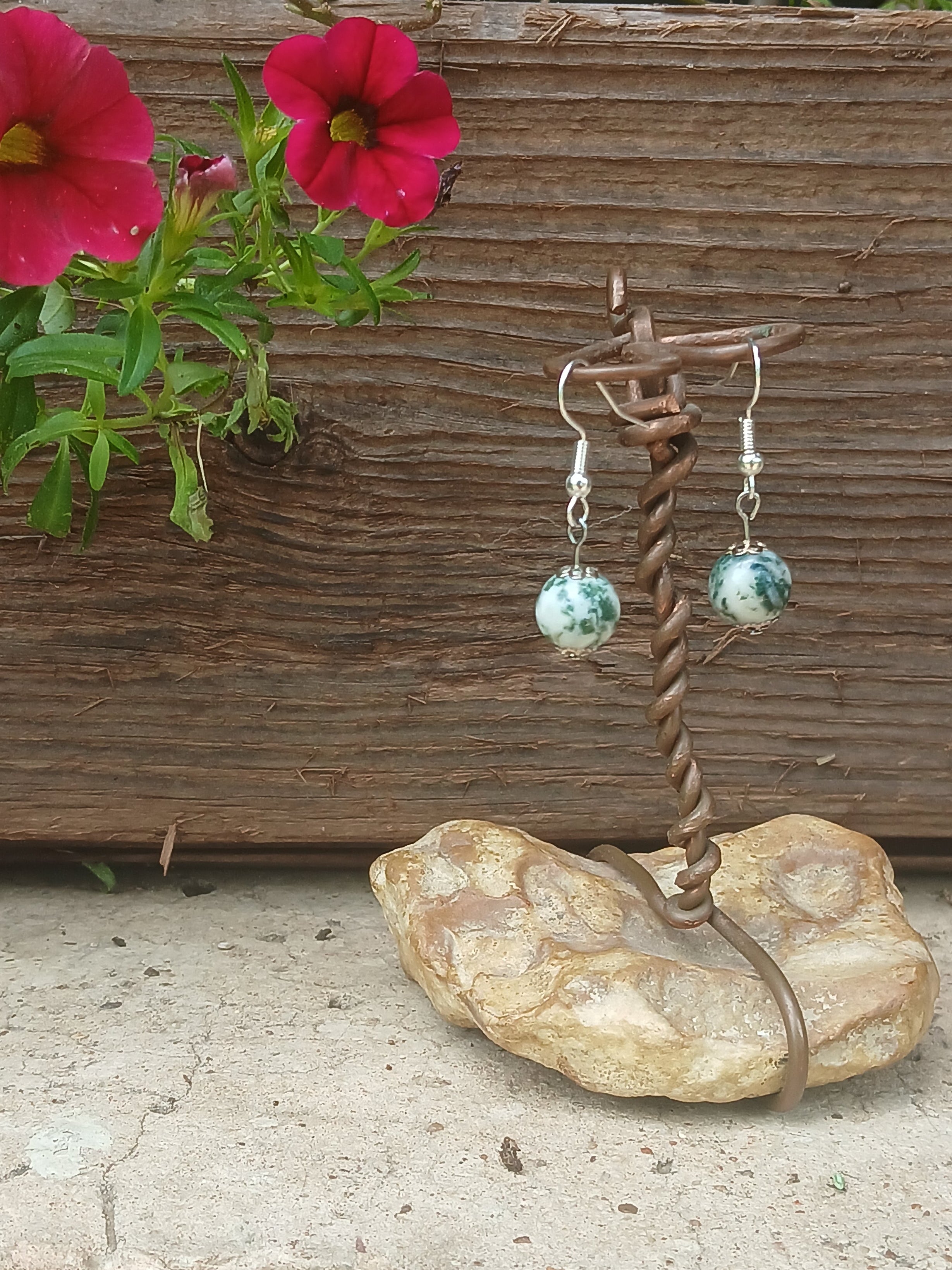 Earrings on a stone stand with pink flowers in the background