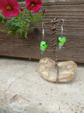 Green heart-shaped earrings on a stone stand with pink flowers in the background