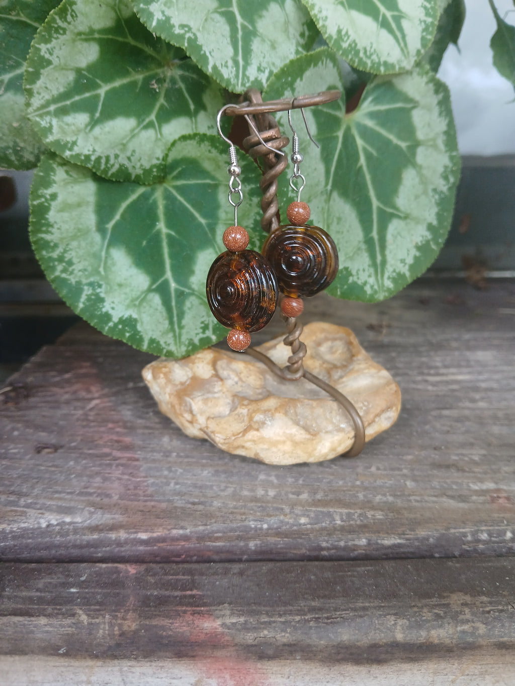 Pair of earrings with brown and orange beads on a rock with green leaves in the background