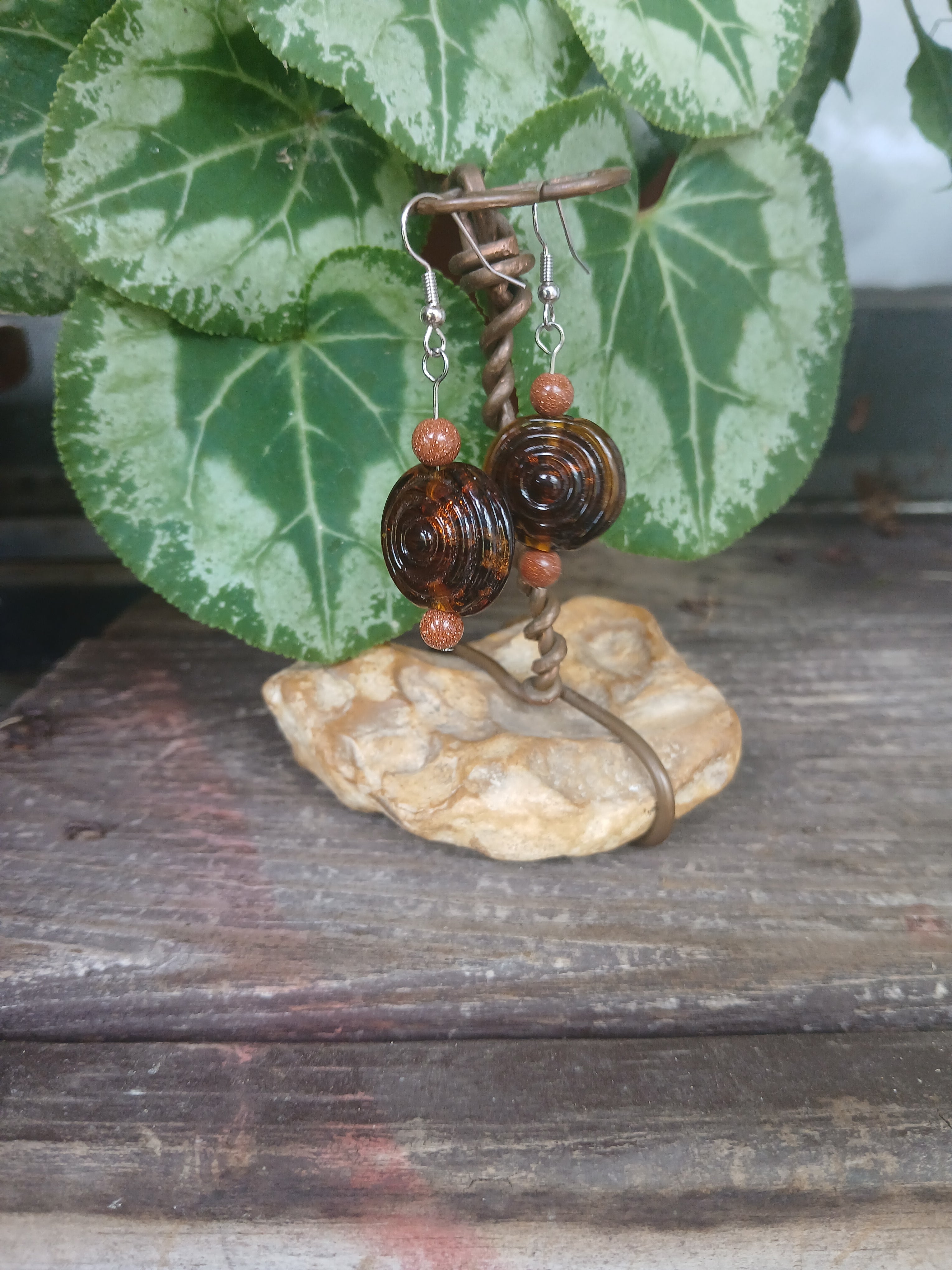 Pair of earrings with brown and orange beads on a rock with green leaves in the background