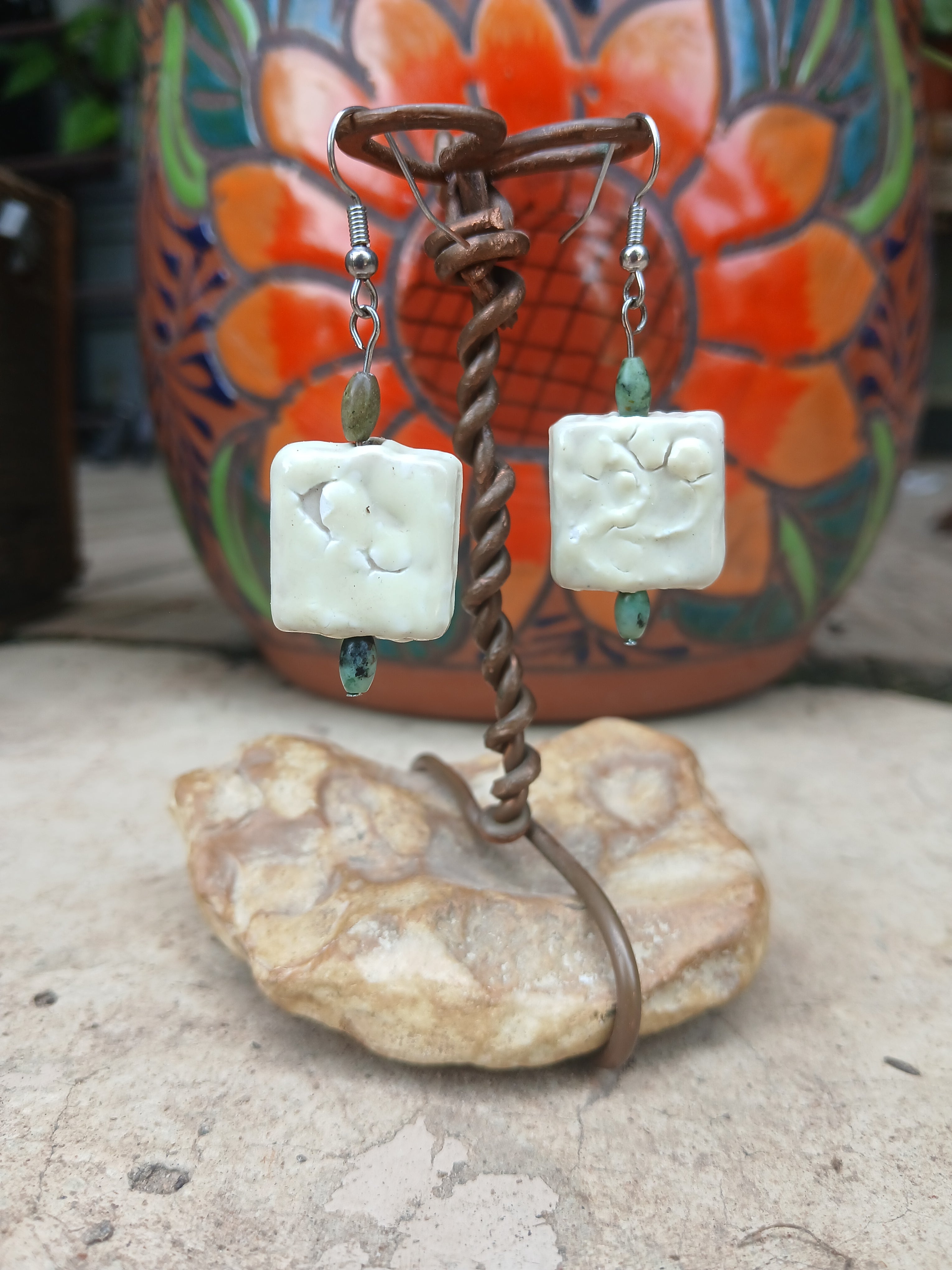 Pair of earrings with white square stones and brown wire on a textured surface.