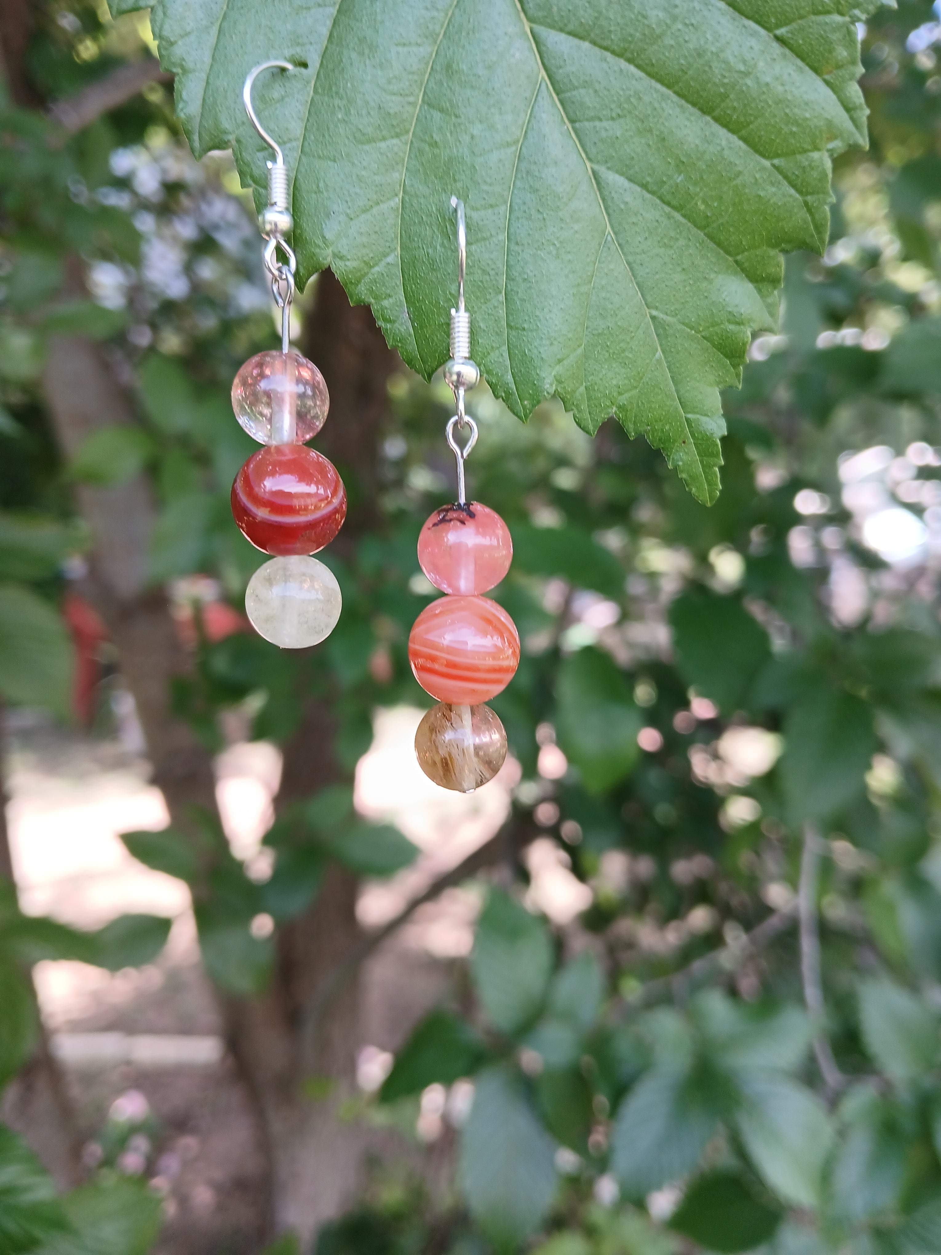 Beaded earrings with red and white beads on a leafy green background