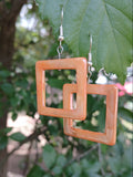 Square-shaped earrings on a blurred green leaf background