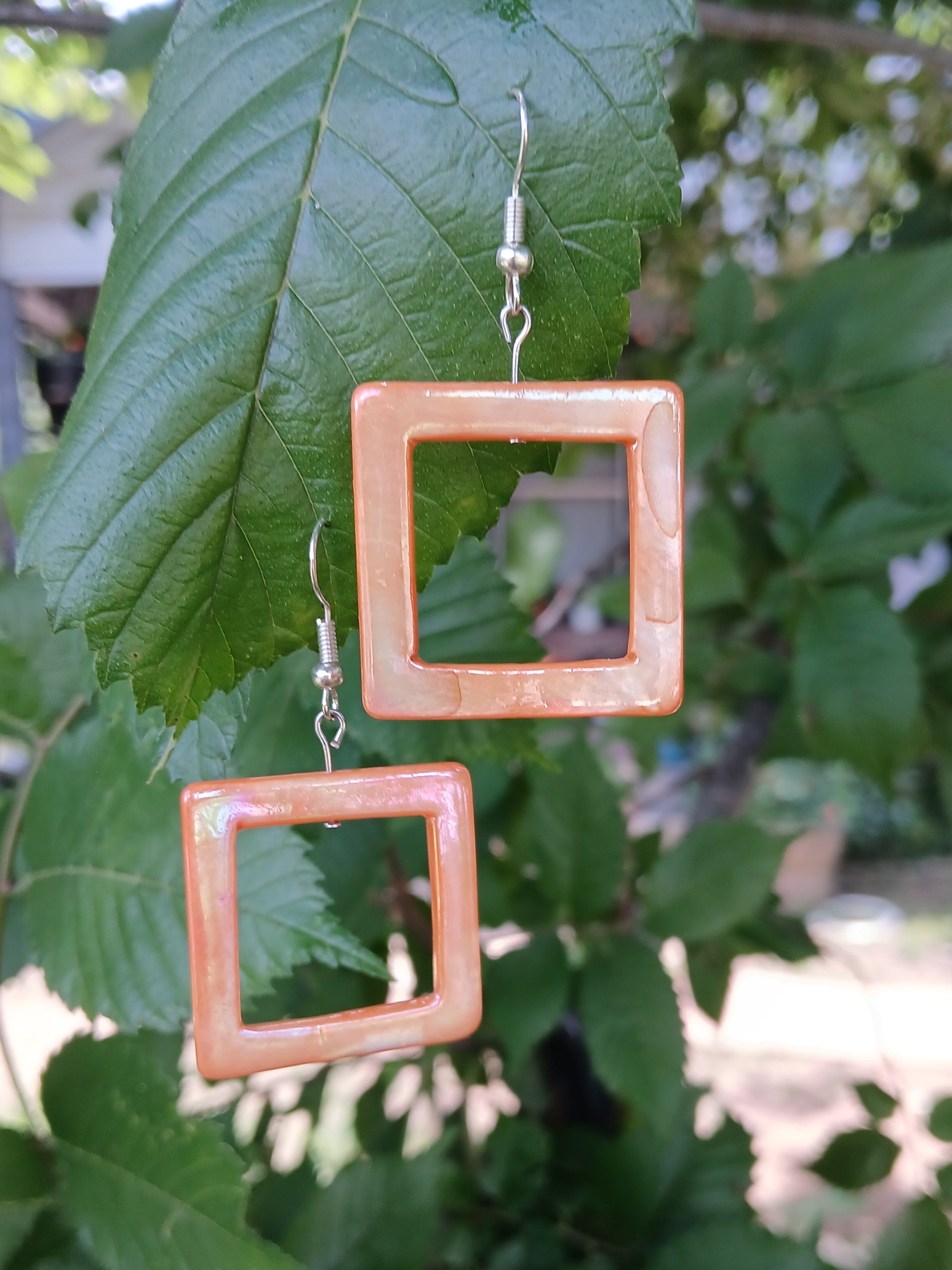 Square-shaped earrings on a green leaf with a blurred natural background