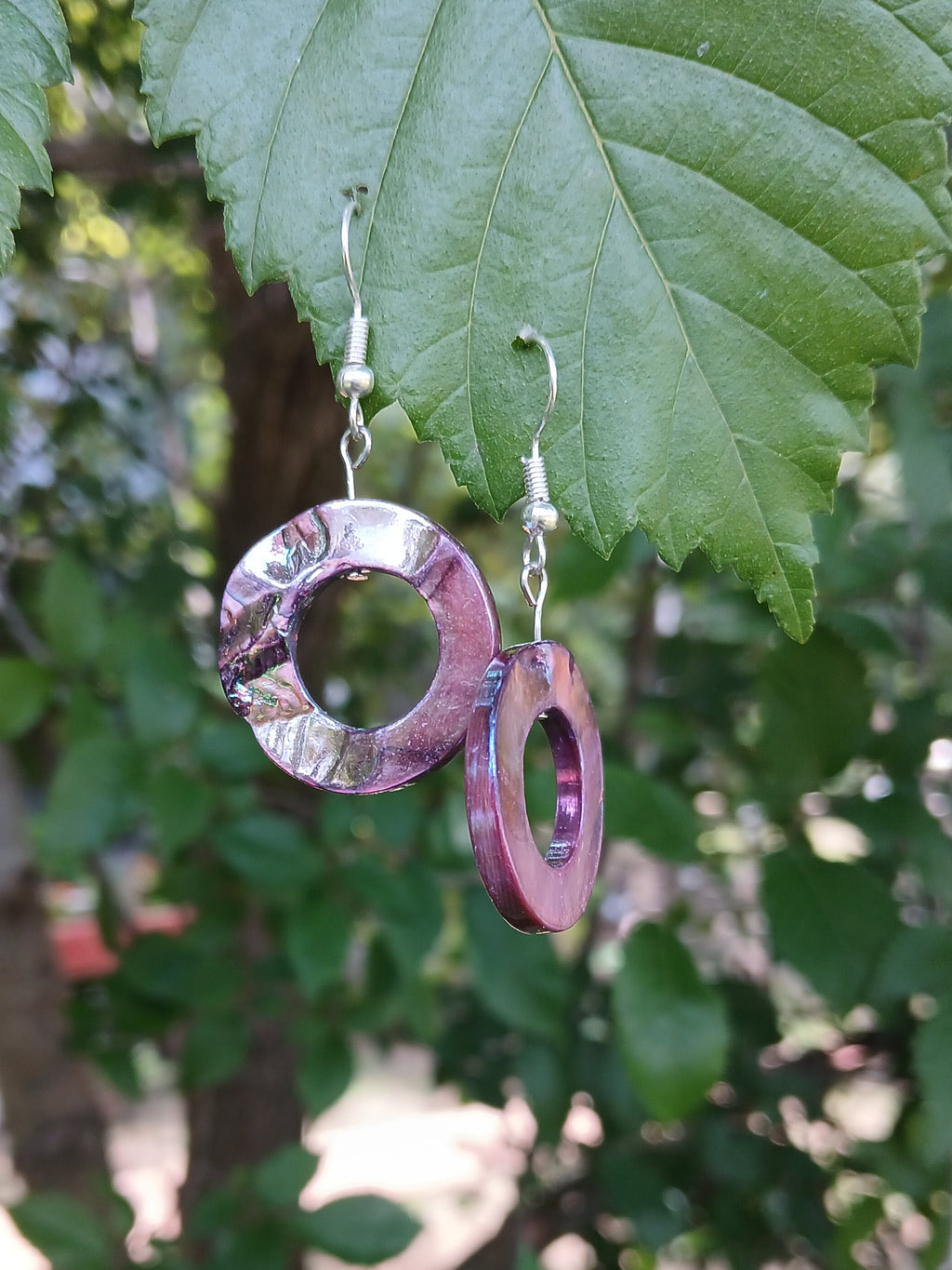 Purple hoop earrings hanging on green leaves with a blurred background