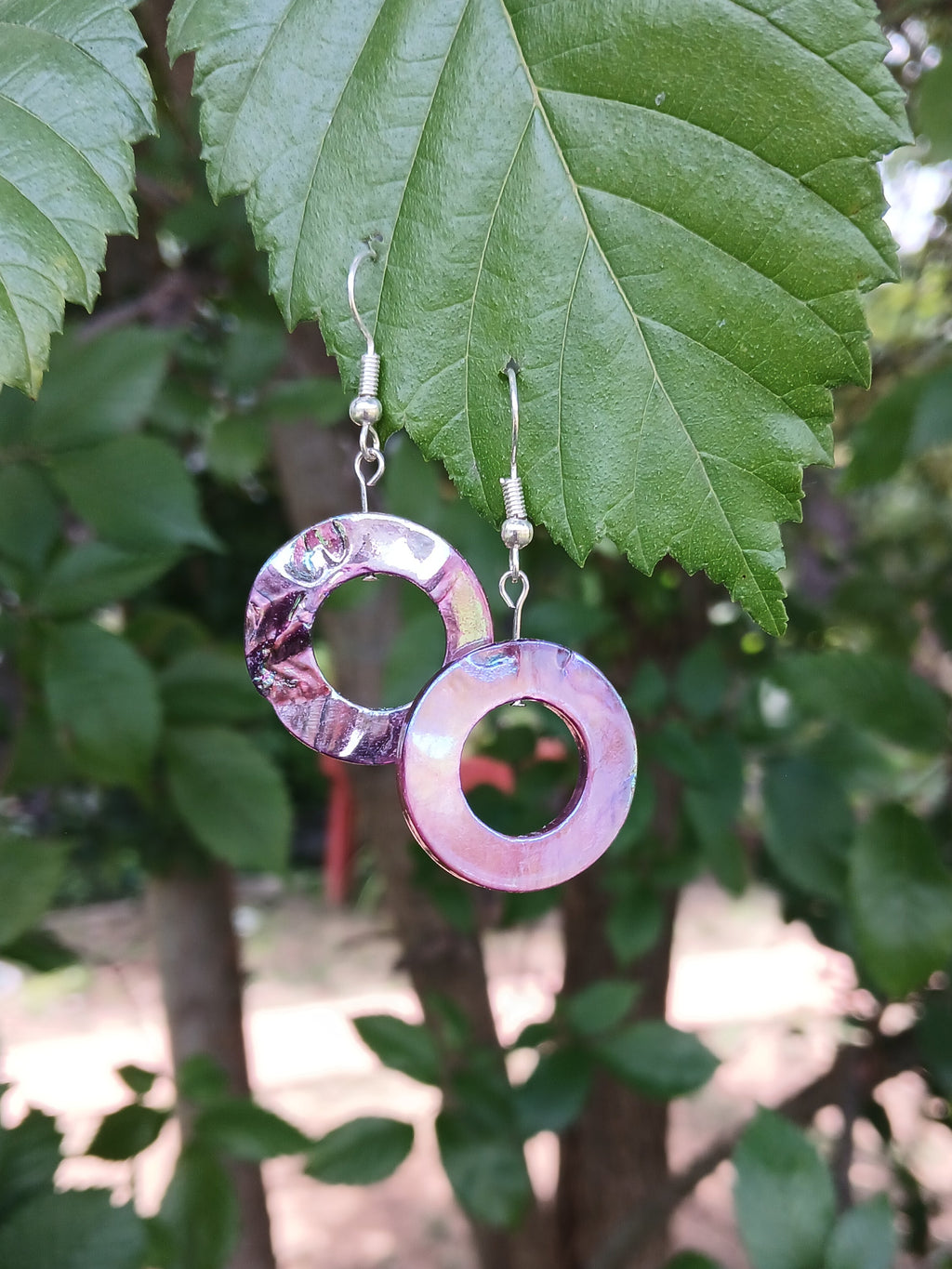 Pink hoop earrings hanging on a green leaf with a blurred natural background