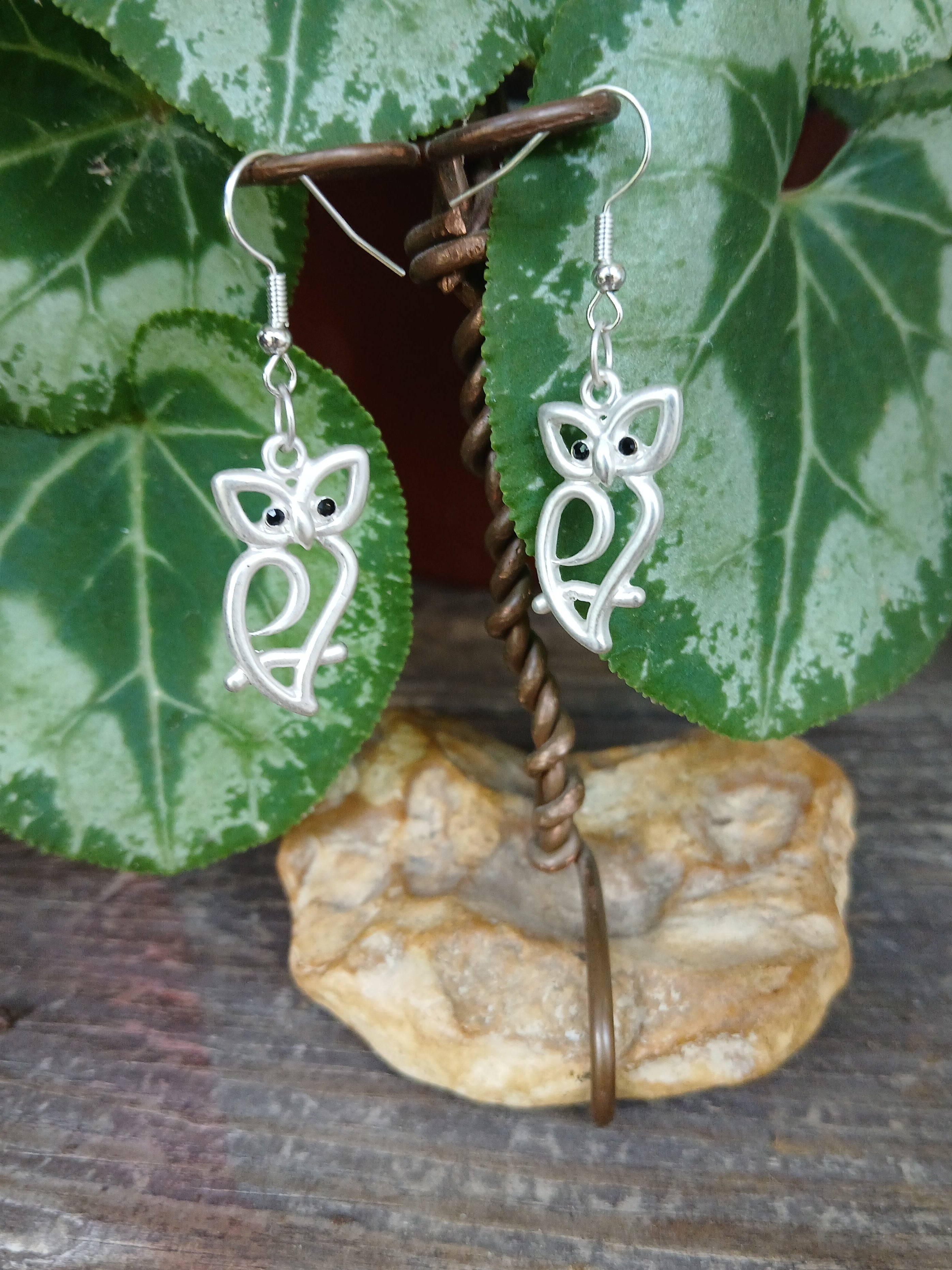 Silver leaf-shaped earrings on a wooden surface with green leaves and a stone.