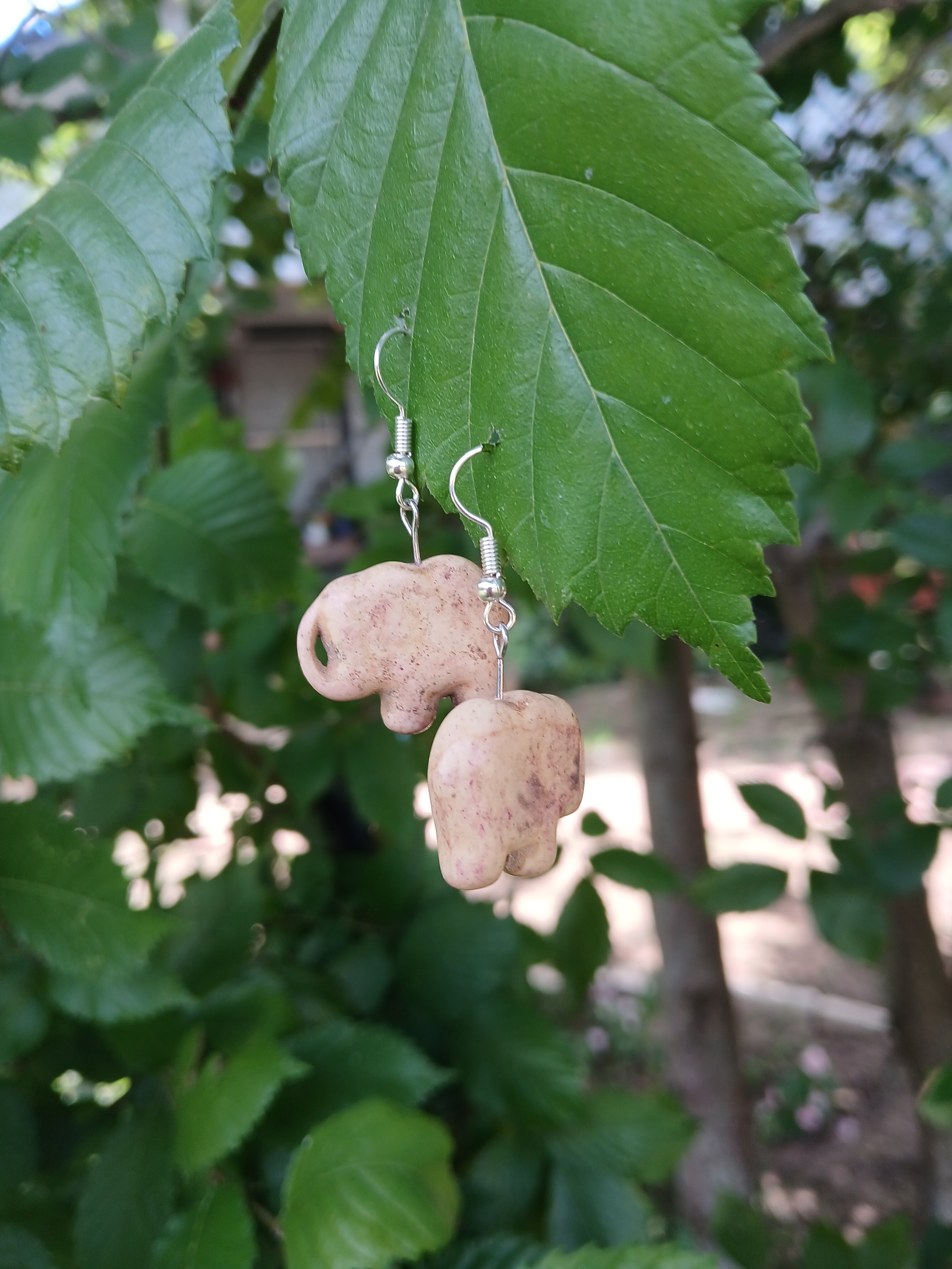 Beige stone earrings on a green leaf with a blurred natural background