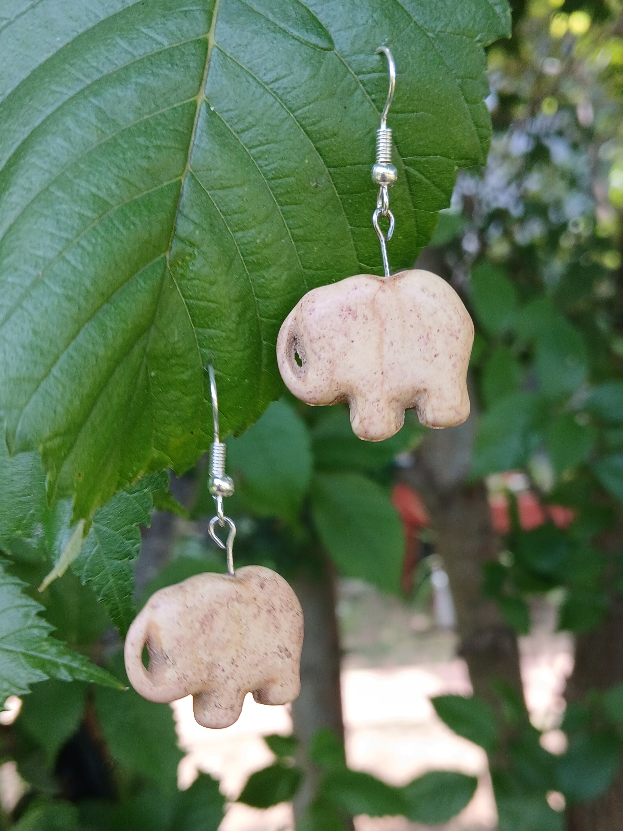 Elephant-shaped earrings hanging from a green leaf