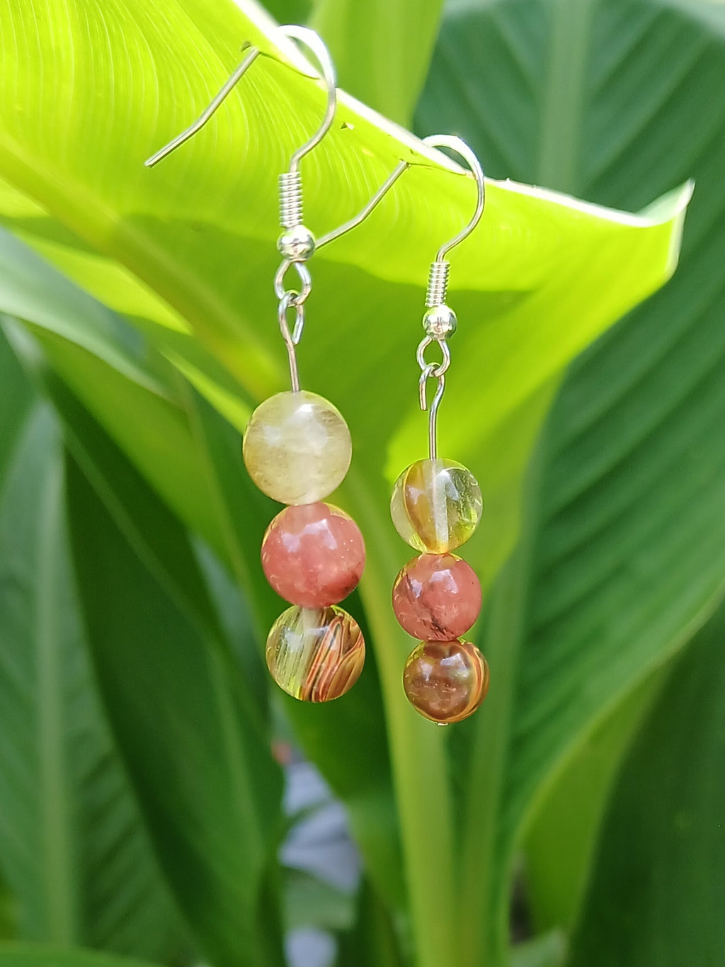 Pair of colorful beaded earrings on a green leafy background