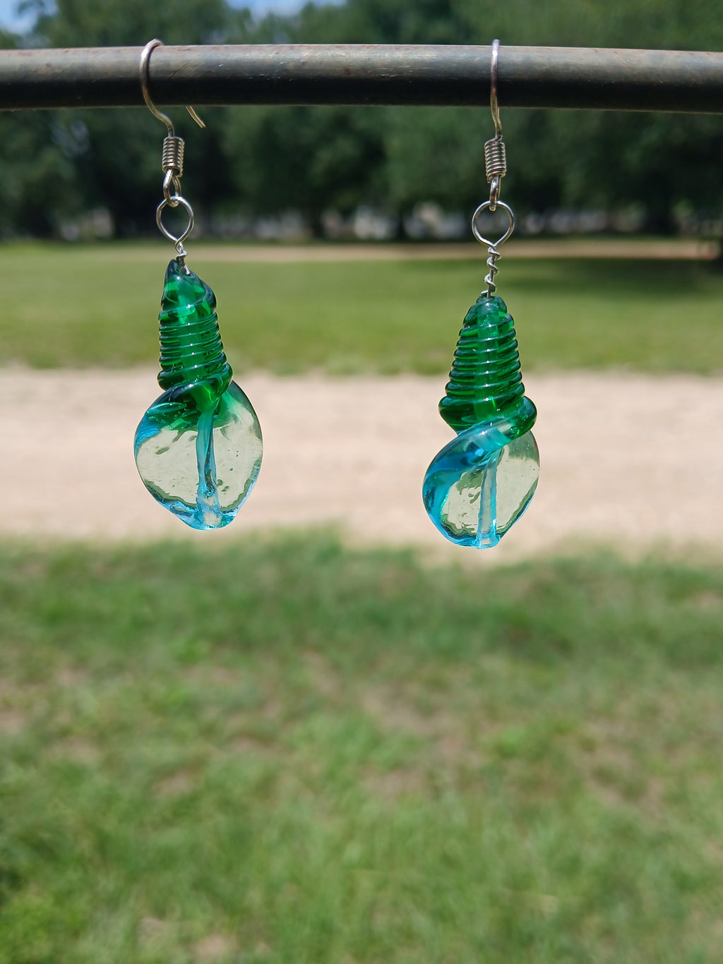 Two green glass bottle stoppers hanging from a wire against a blurred natural background.