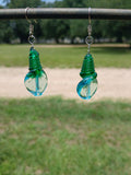 Two green glass bottle stoppers hanging from a wire against a blurred natural background.