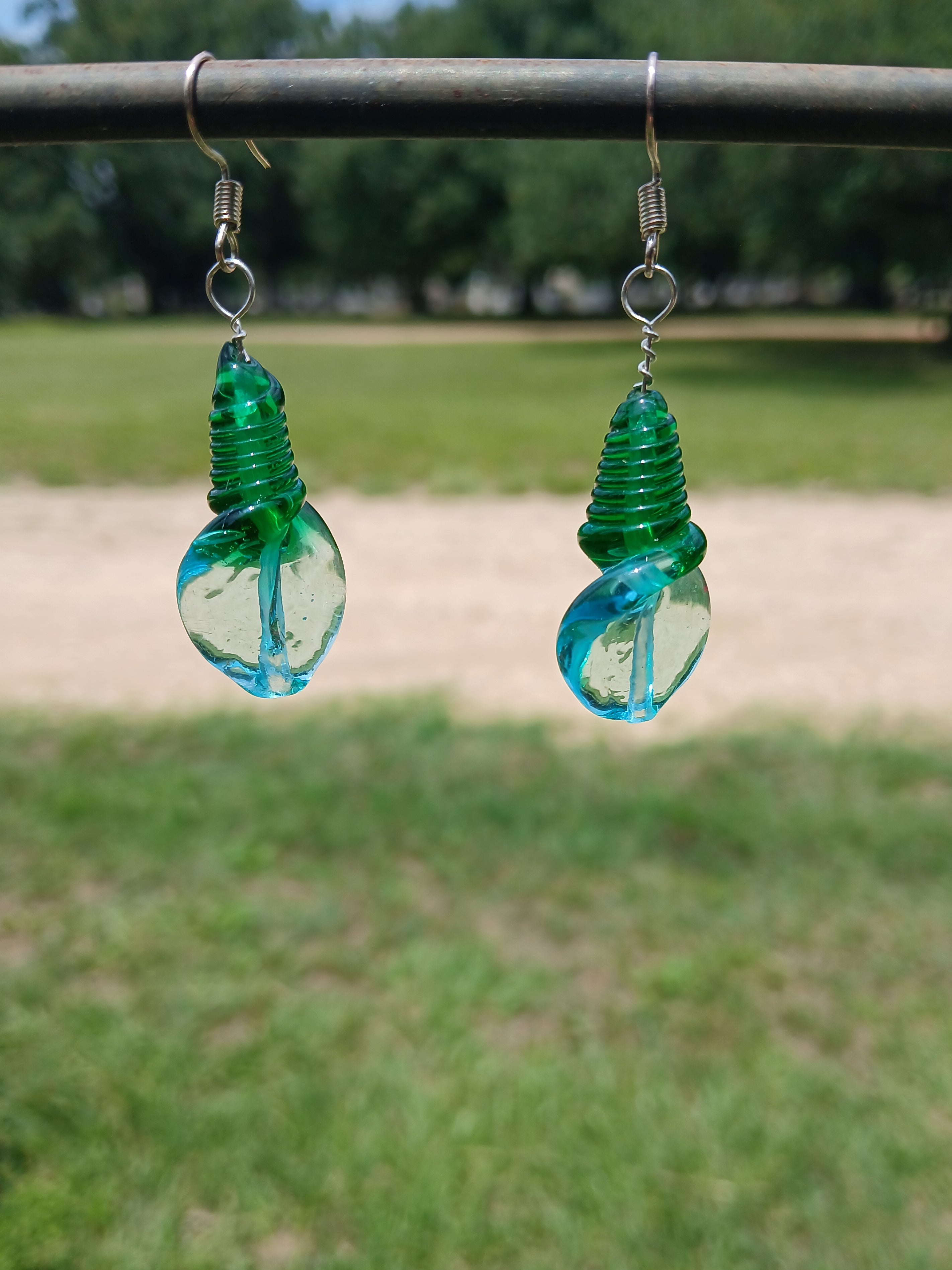 Two green glass bottle stoppers hanging from a wire against a blurred natural background.