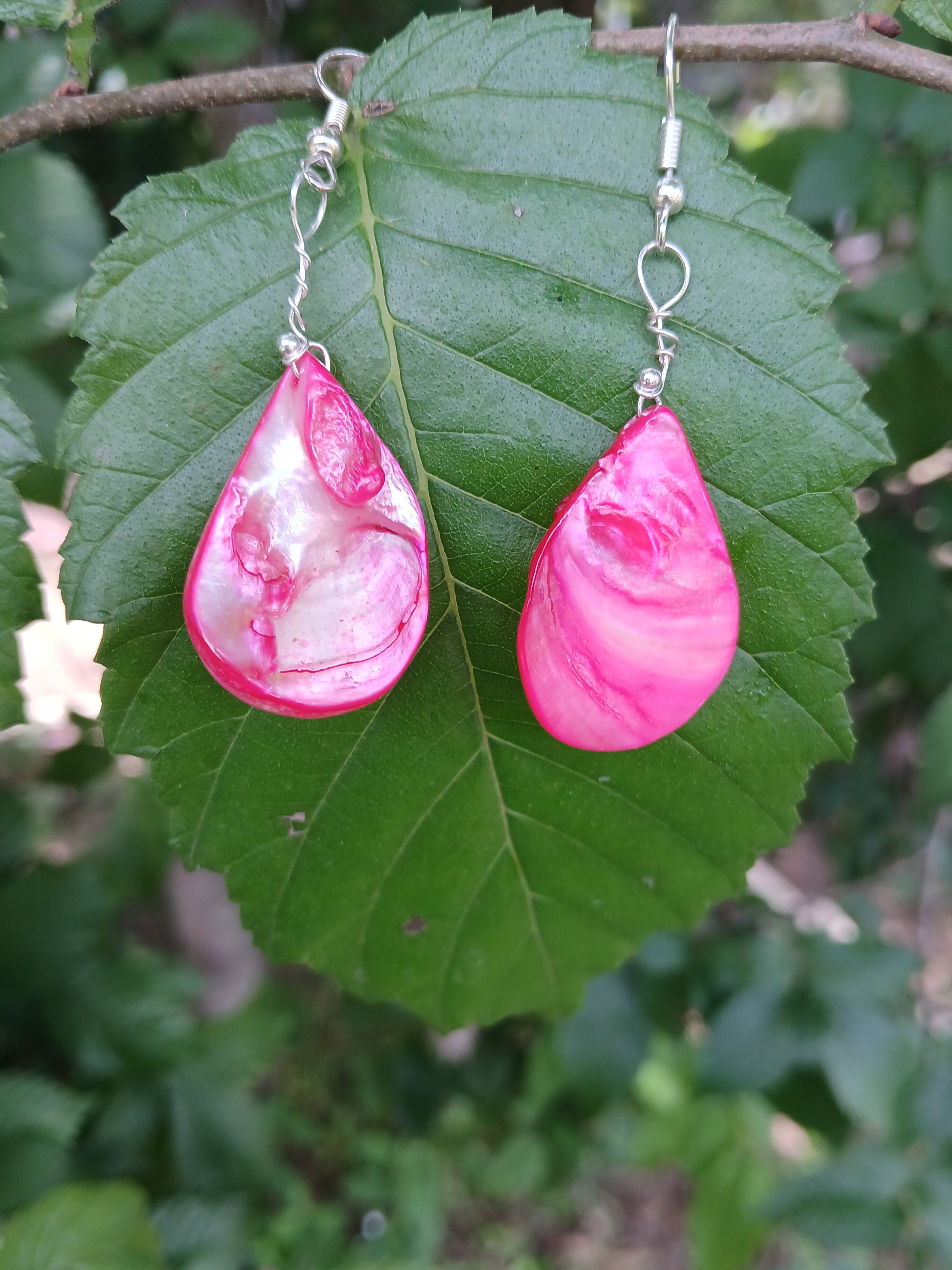Pink teardrop earrings on a green leaf with a natural background