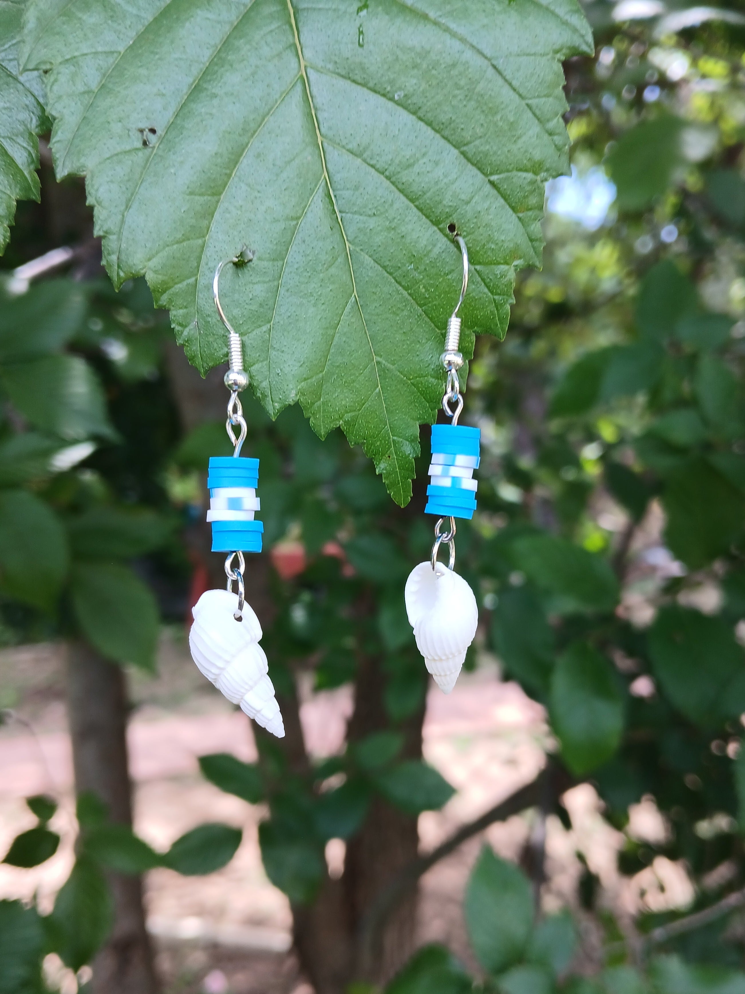Pair of earrings with blue and white beads on a leafy background