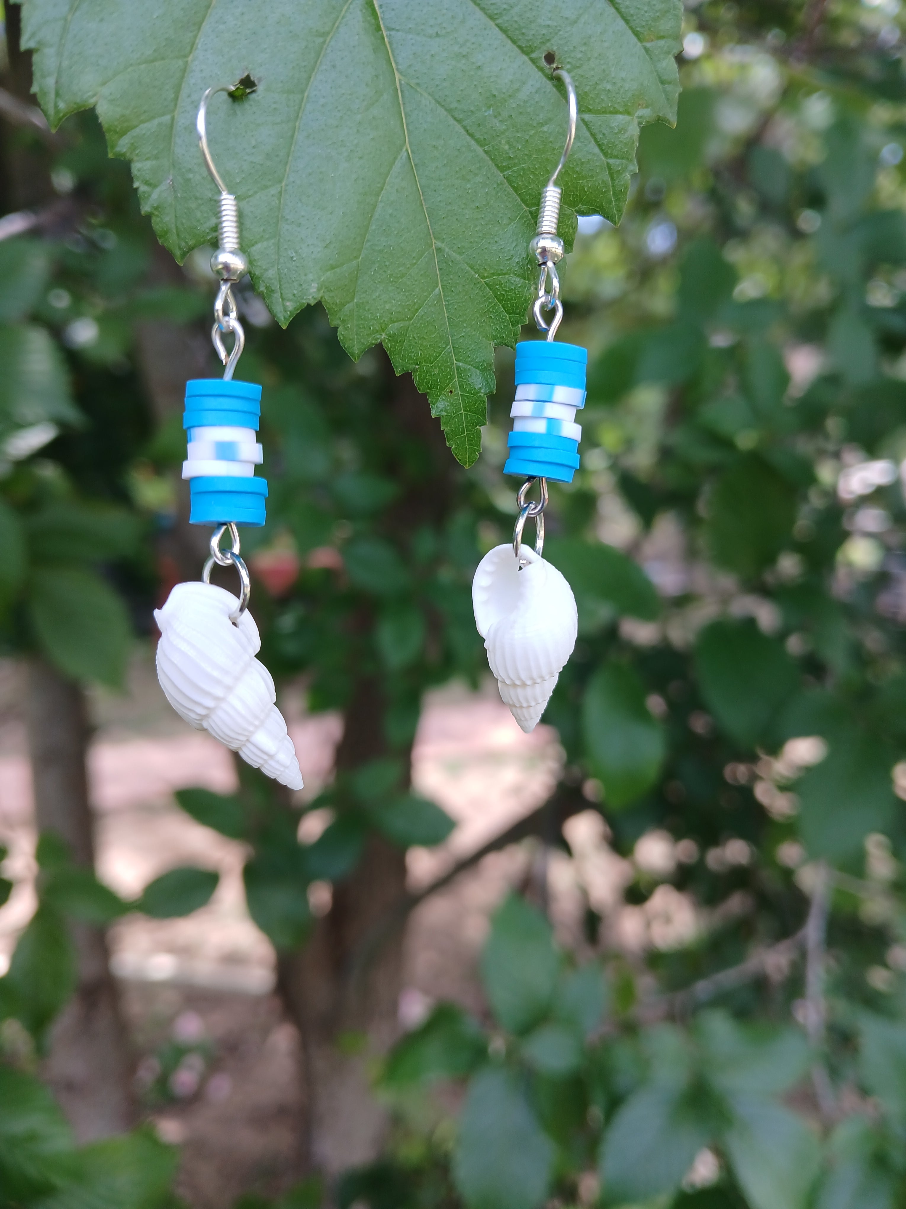 Pair of earrings with blue and white beads and shell-like elements on a leaf.