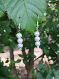 Silver beaded earrings on a green leaf with a blurred natural background