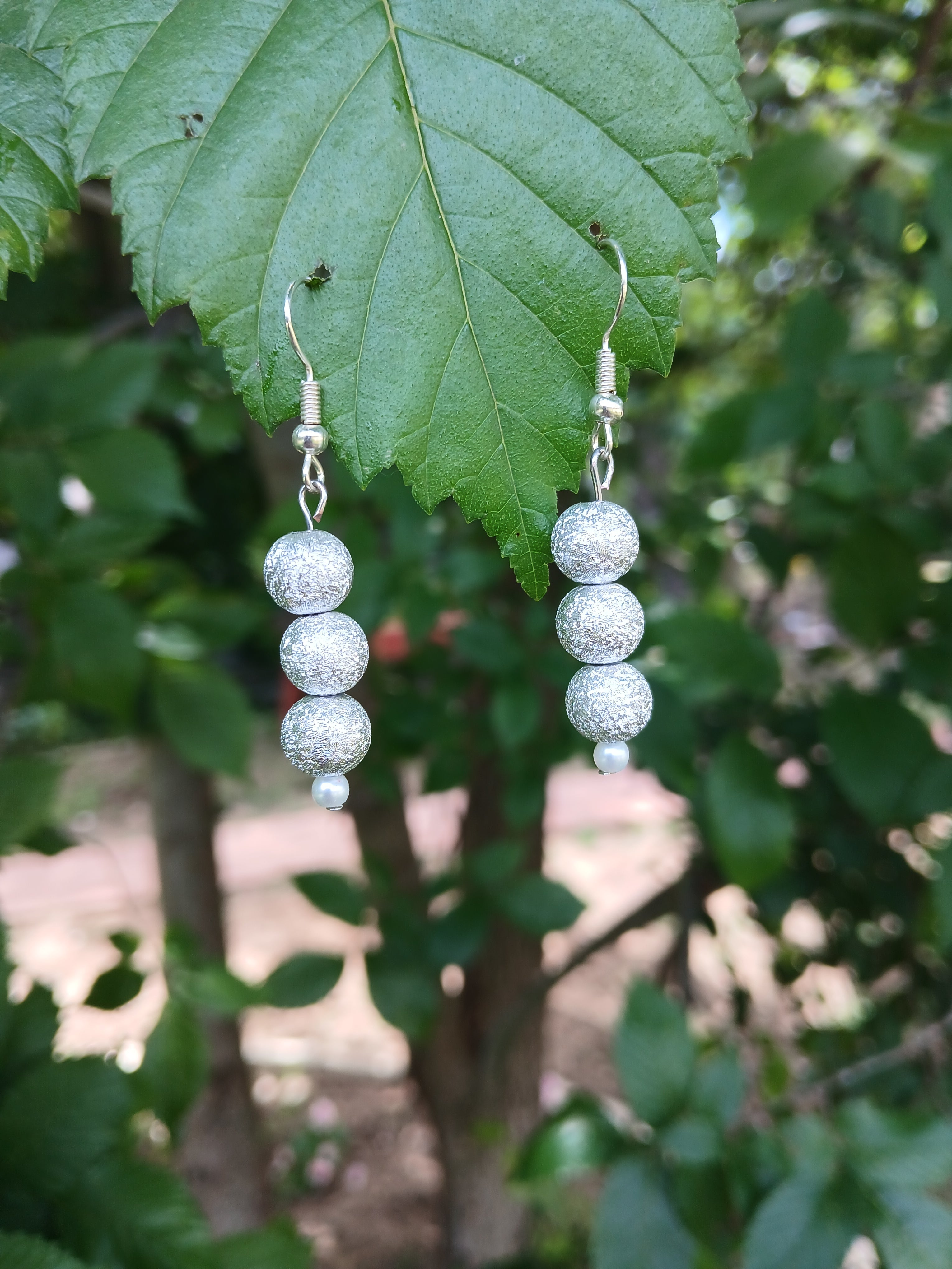 Silver beaded earrings on a green leaf with a blurred natural background