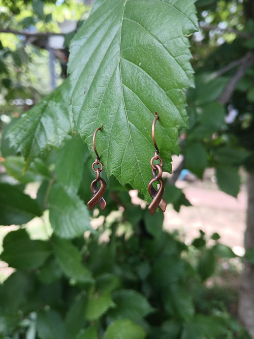 Decorative copper bracelet on a green leaf with blurred foliage background