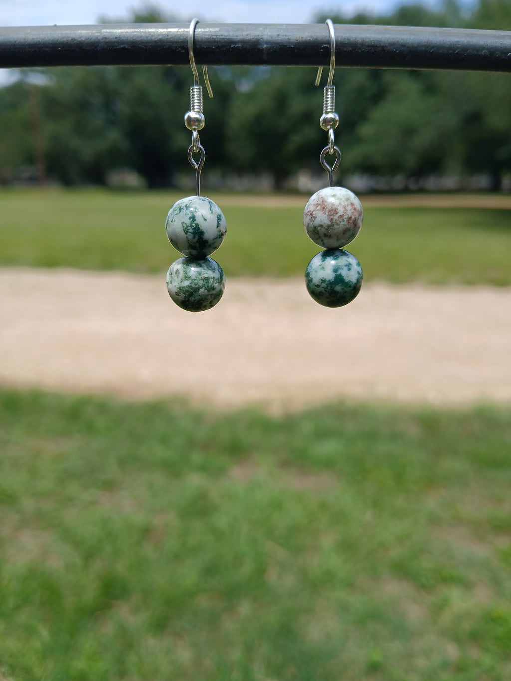 Pair of earrings with green and white marbled beads displayed against a blurred natural background.