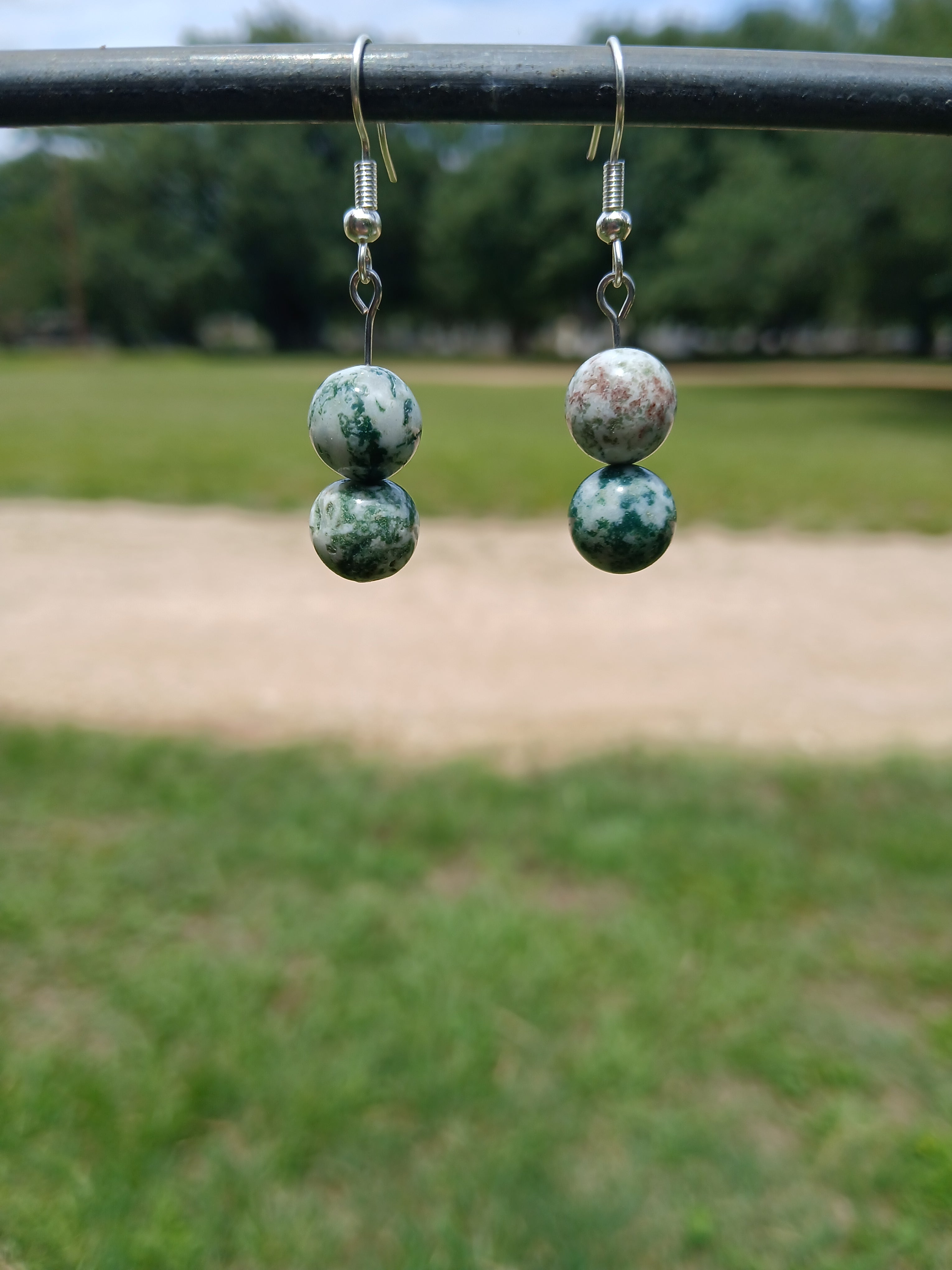 Pair of earrings with green and white marbled beads displayed against a blurred natural background.